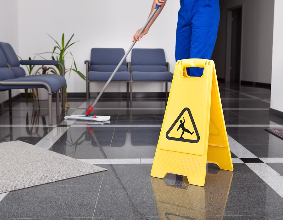 Bodenreinigung mit Wischmopp in einem Bürogebäude, daneben ein gelbes Warnschild