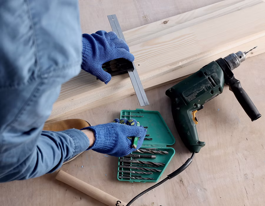 Handwerker mit Arbeitshandschuhen bereitet Bohrmaschine und Werkzeug für Reparaturarbeiten vor